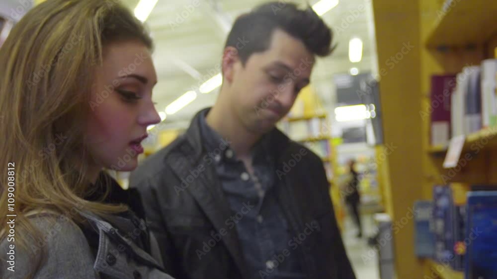 Camera moves across a handsome man and beautiful girl on a date flipping through a book, chatting, and laughing Camera moves across a handsome man and beautiful girl on a date flipping through a book, chatting, and laughing