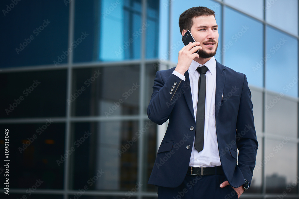 Portrait of businessman talking on cell phone against the building with a glass facade Portrait of businessman talking on cell phone against the building with a glass facade