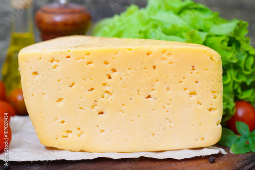 Tilsit Tilsiter cheese of the semi-hard cheese with vegetables on a wooden background