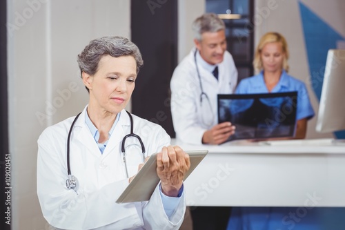 Female doctor using digital tablet with colleague checking X-ray