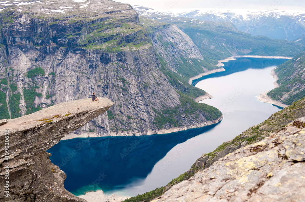 man sits on the edge of a cliff and looks at mountain lake (Trol