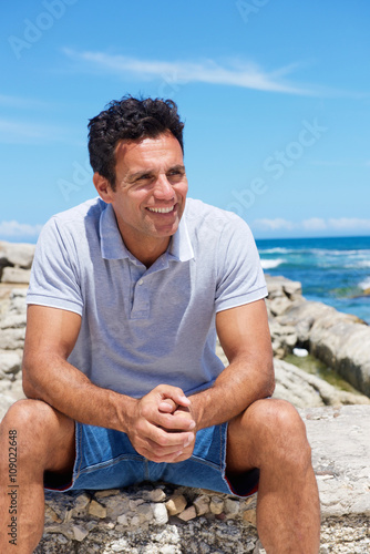 Smiling middle aged man sitting by the beach