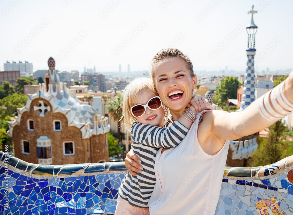 Smiling mother and baby taking selfie at Park Guell, Barcelona - obrazy, fototapety, plakaty 