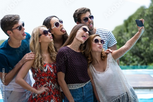 Happy friends taking a selfie near swimming pool