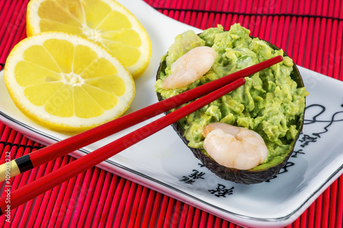 Bild auf Leinwand Tasty avocado salad with shrimps, lemon and red chopsticks on the white plate