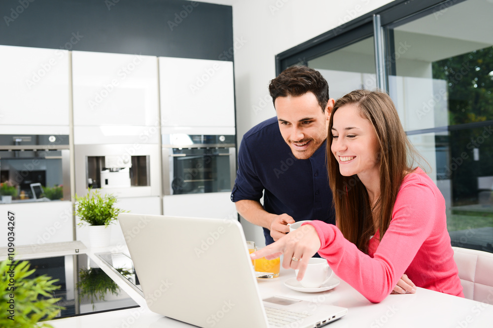 young couple at home having coffee in kitchen and working on laptop computer young couple at home having coffee in kitchen and working on laptop computer