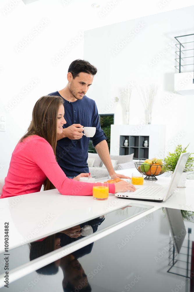 young couple at home having coffee in kitchen and working on laptop computer young couple at home having coffee in kitchen and working on laptop computer