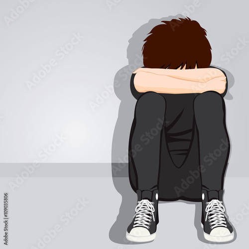 Sad teenager boy desperate hiding her face sitting on floor on grey background with dark clothes