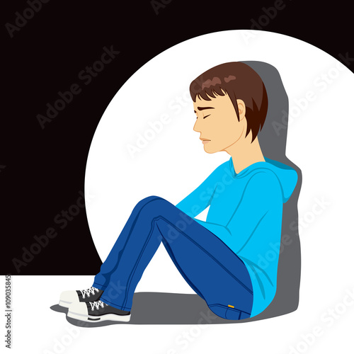 Sad teenager boy crying sitting on floor under white spot light on dark background