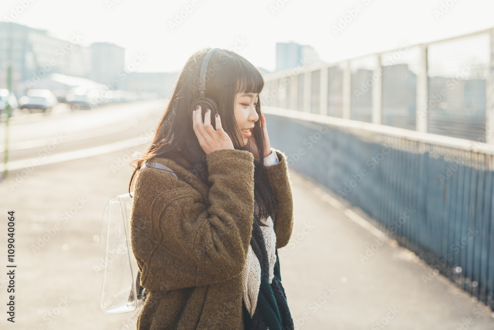 Half length of young beautiful asian hipster woman in the city back light listening music with headphones, eyes closed, smiling - music, technology, relax concept