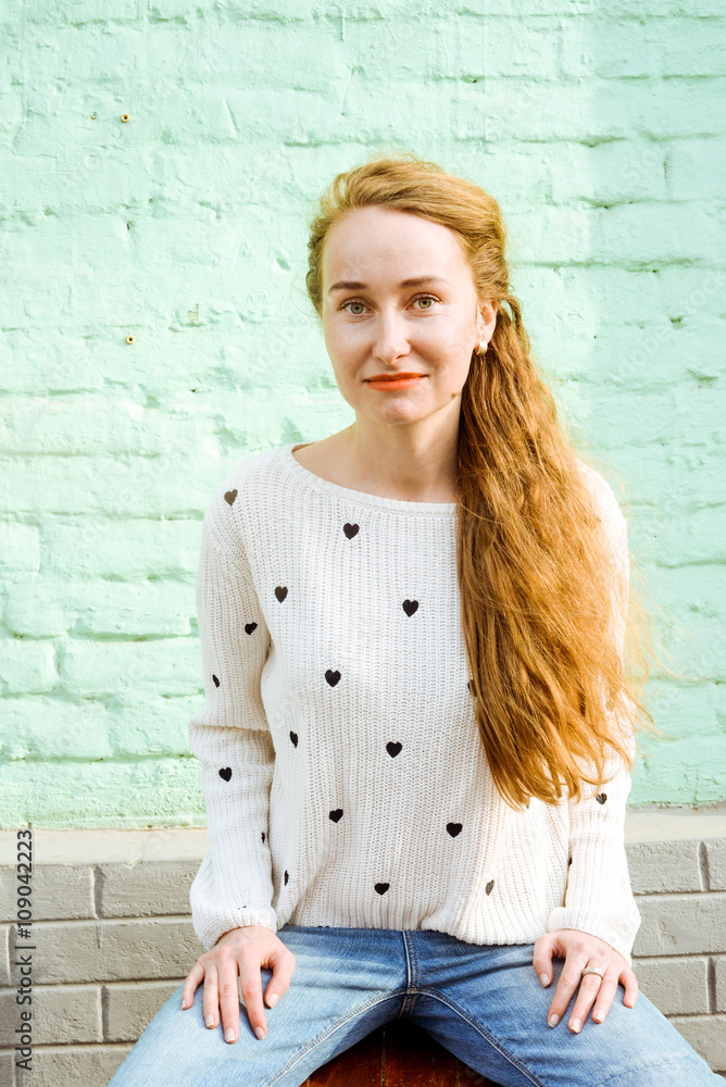 Young beautiful long-haired hipster girl sitting on a sunny day outdoors. Lifestyle portrait of a woman dressed in colorful sweater with city in the background. Concept of freedom and happiness. Young beautiful long-haired hipster girl sitting on a sunny day outdoors. Lifestyle portrait of a woman dressed in colorful sweater with city in the background. Concept of freedom and happiness.