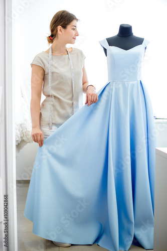 pretty young girl adjusts  dress on the mannequin. blue dress on a mannequin. seamstress in a sewing workshop
