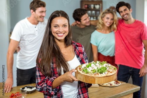 Happy young woman holding pizza with friends at home