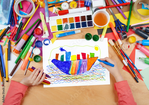 child drawing ocean liner ship, top view hands with pencil painting picture on paper, artwork workplace