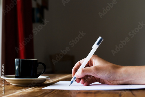 Hand writing with a pen. Coffee at a wooden table. Selective focus.