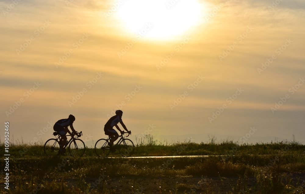 Two cyclists riding bicycle on sunset sky, silhouette.