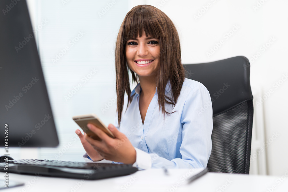 Woman using her cellphone in front of her desktop computer Woman using her cellphone in front of her desktop computer