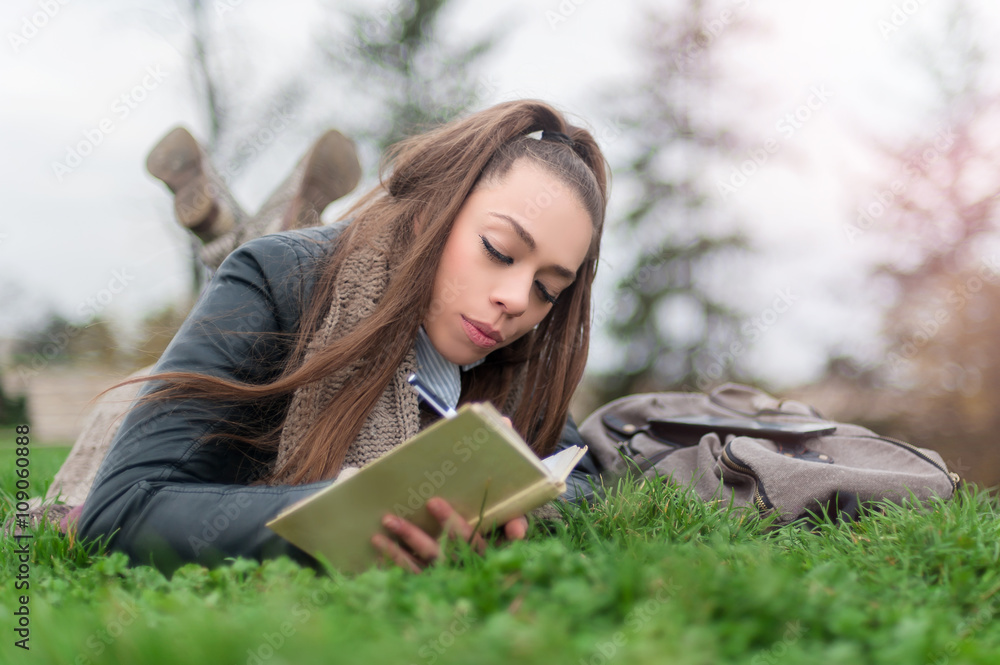Obraz premium Beautiful girl writing in a book / Girl student in park writes in writing book