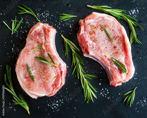 Фотография Raw pork steaks with rosemary on black stone background