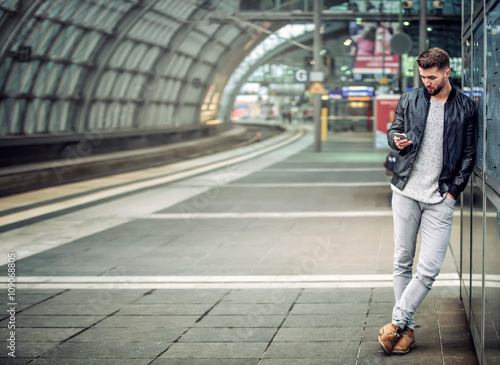 Junger Mann mit Smartphone im Bahnhof