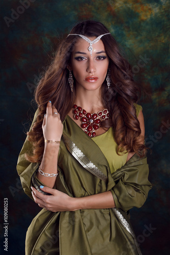 Beautiful woman in green indian sari and jewelry on colorful bac