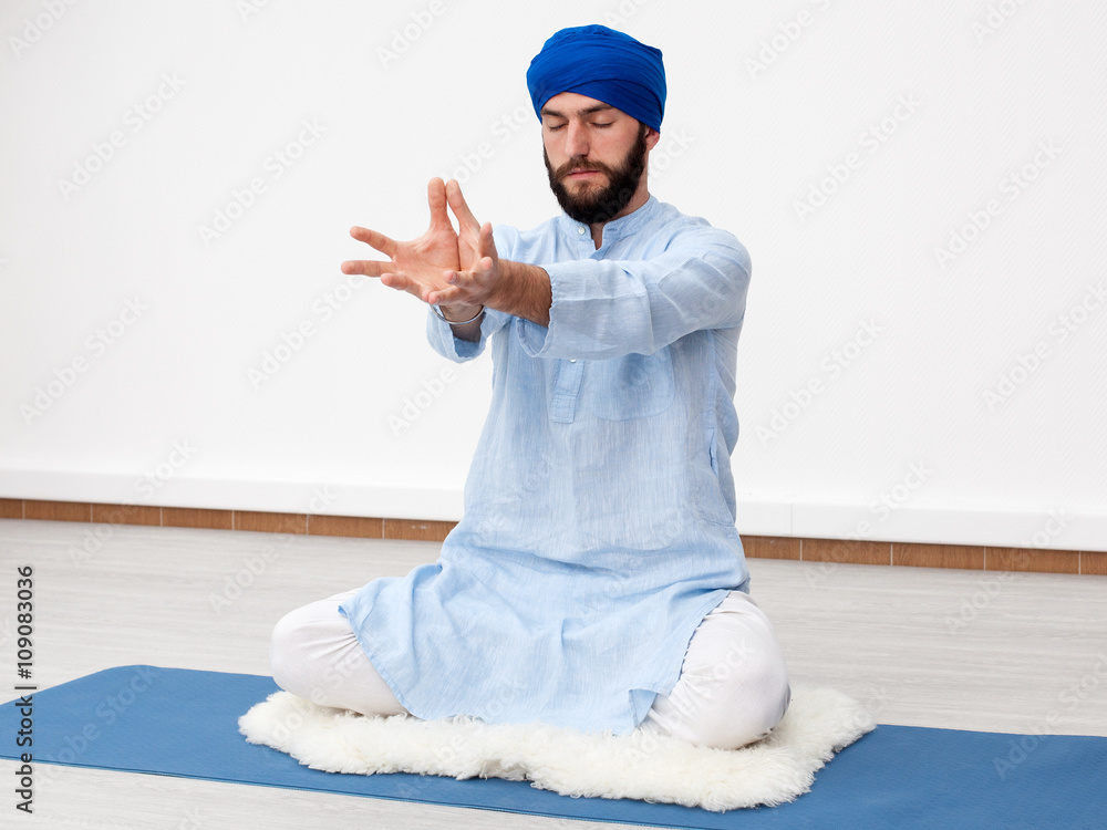 Meditation. Portrait of a young bearded yogi man in a turban with hands  folded in mudra on the chest level, sitting on the sheep skin in a  meditative pose Stock Photo