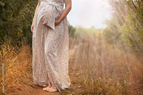 The pregnant woman in the summer in a long dress on the forest road