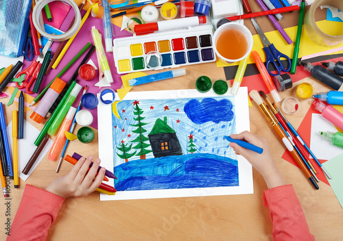 child drawing christmas night in forest with house   top view hands with pencil painting picture on paper  artwork workplace