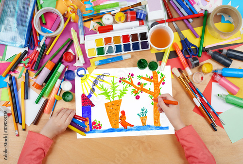 child drawing rabbit with carrot on kitchengarden near house, top view hands with pencil painting picture on paper, artwork workplace