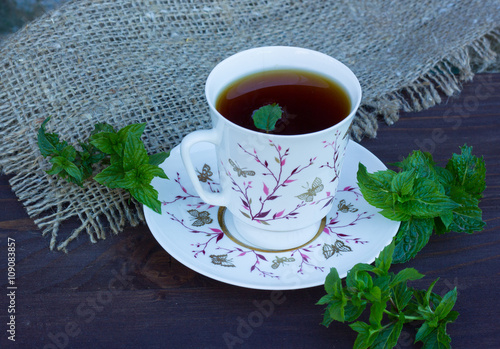 На фото изображена чашка с чаем и листья мяты