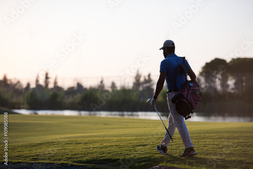 golfer walking and carrying golf bag at beautiful sunset