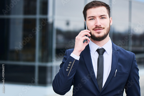 Portrait of businessman talking on cell phone against the building with a glass facade