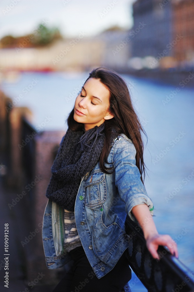 beautiful girl with long hair in a scarf closed her eyes with happiness near the parapet on the embankment