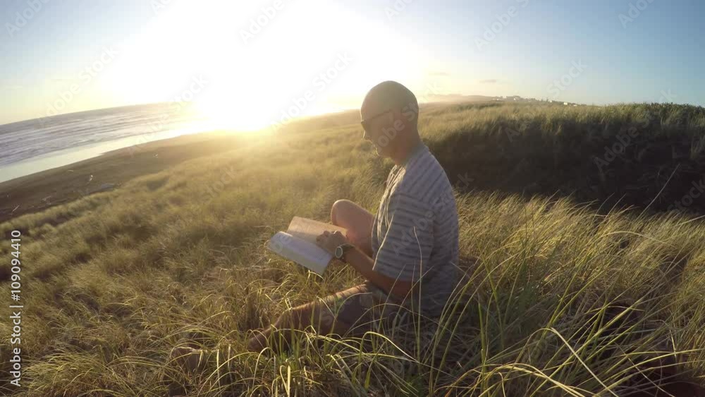 Man sitting in sand dunes reading book and laughing Man sitting in sand dunes reading book and laughing