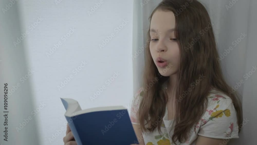 Emotional little girl reading an interesting book by window. Emotional little girl reading an interesting book by window.