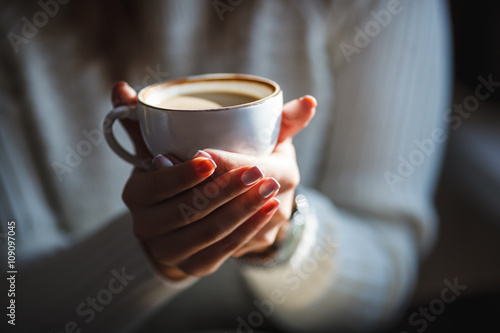 Woman holds hot cup of coffee, warming her hands