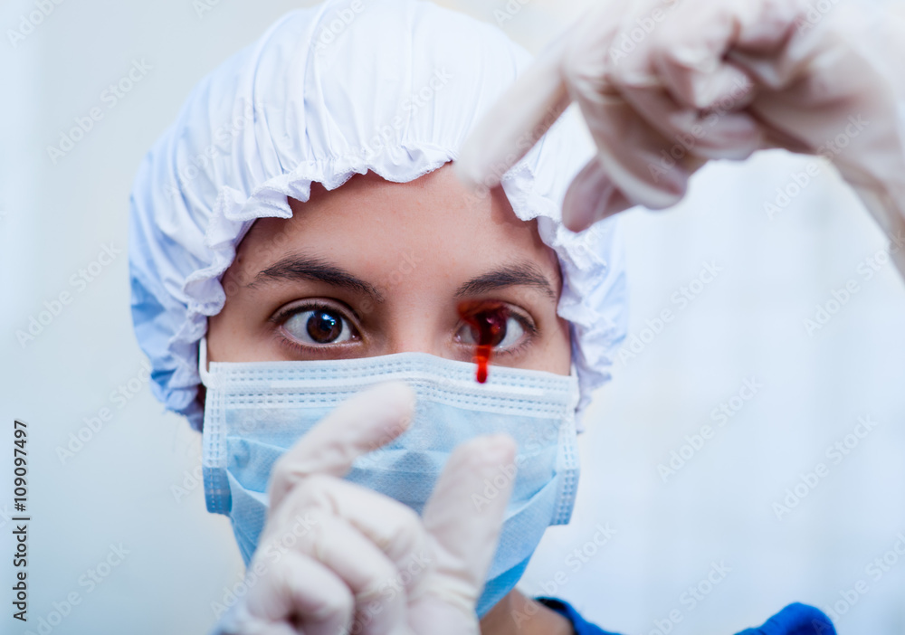 Closeup headshot nurse wearing bouffant cap and facial mask holding up blood sample on slide glass for camera Closeup headshot nurse wearing bouffant cap and facial mask holding up blood sample on slide glass for camera