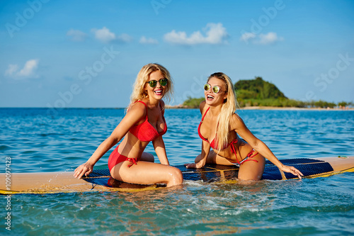 Pretty female friends having fun on a surfboard in the sea