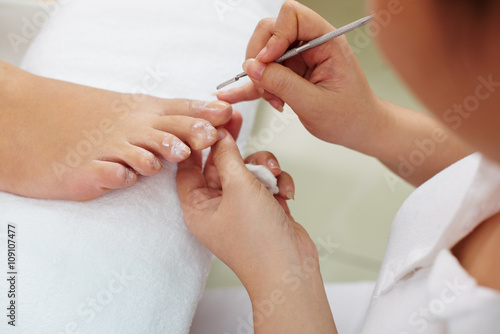 Woman receiving pedicure by beautician in nail salon