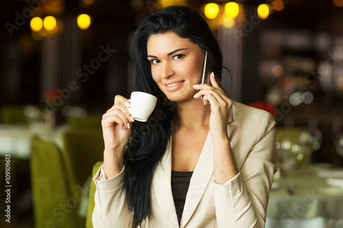a young beautiful girl drinking coffee in a restaurant talking on the phone