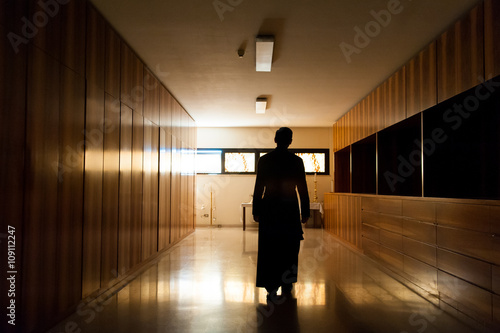 Fototapeta Shadow of young priest dressed in black walking alone in dark moody church