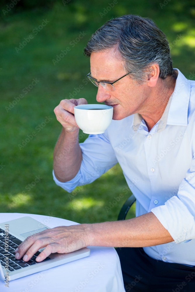 Casual businessman using laptop and having coffee sitting on a terrace Casual businessman using laptop and having coffee sitting on a terrace