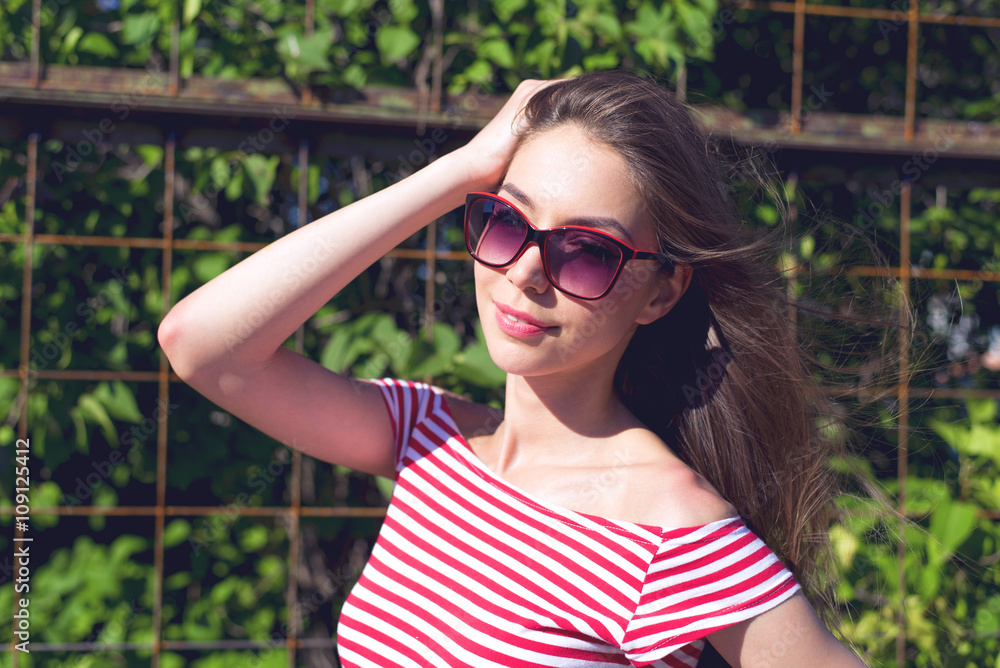 Beautiful girl in a bright red T-shirt, fashion lifestyle, posing against the backdrop of fence with green leaves Beautiful girl in a bright red T-shirt, fashion lifestyle, posing against the backdrop of fence with green leaves