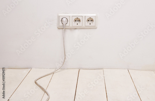 Three white electrical outlets with white power cord and plug on white wall. © lizmyosotis