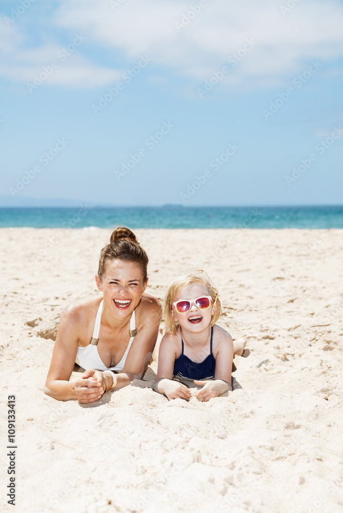 Happy mother and child in swimsuits laying on sandy beach Happy mother and child in swimsuits laying on sandy beach