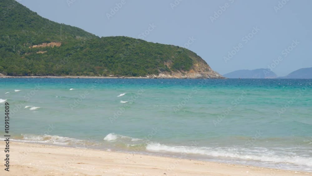 Serene view of sandy beach, sea with small waves and woody mountain on horizon Serene view of sandy beach, sea with small waves and woody mountain on horizon