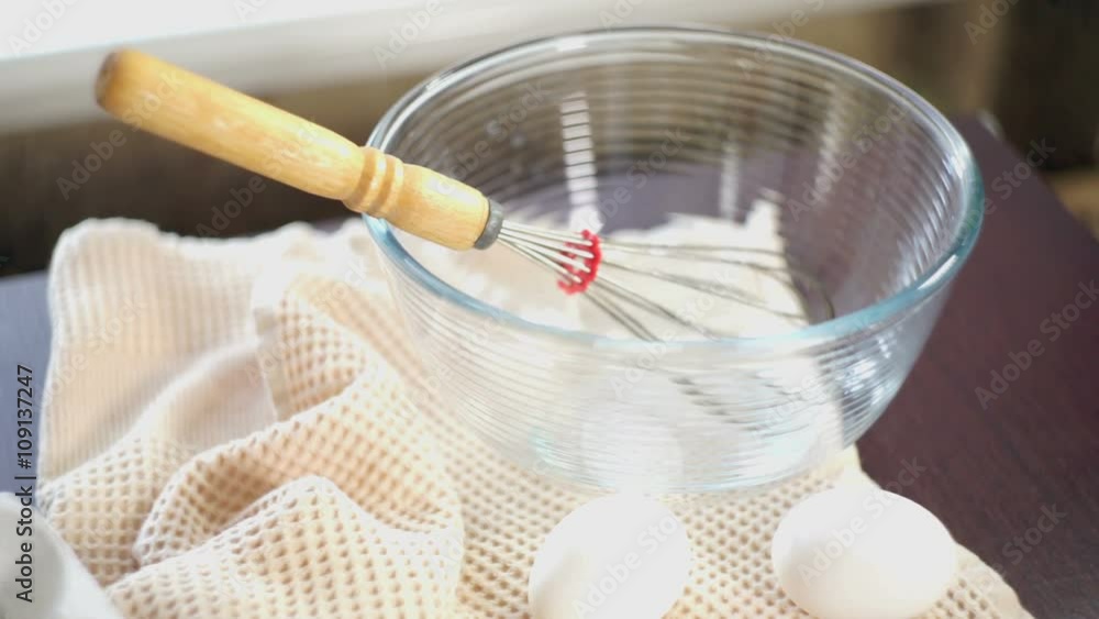 Whisk in glas bowl. Closeup. Eggs on kitchen table. Ingredients for cake baking. Hand throws whisk in a bowl. Food cooking equipment. Preparation for food cooking. Ingredients for baking cake Whisk in glas bowl. Closeup. Eggs on kitchen table. Ingredients for cake baking. Hand throws whisk in a bowl. Food cooking equipment. Preparation for food cooking. Ingredients for baking cake