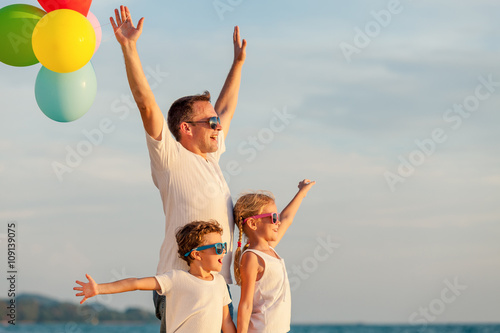 Father and children with balloons playing on the beach at the da