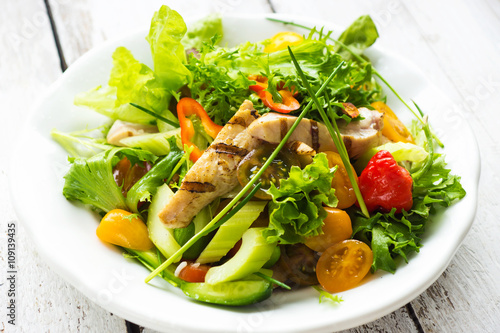 Delicious salad with grilled chicken breast on a wooden background