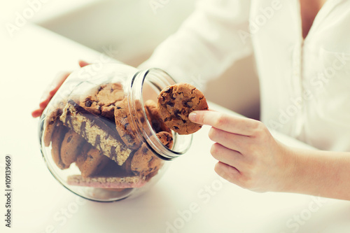 Leinwand Poster close up of hands with chocolate cookies in jar